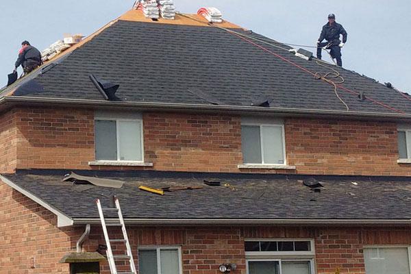 Roofers tearing off old shingles on a brick house