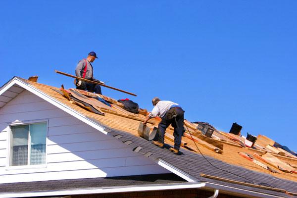Two roofers working on a shingle repair with tools and materials on the roof