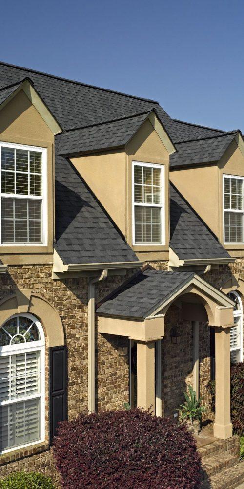 Close-up of a brick house with dormer windows and a new asphalt shingle roof